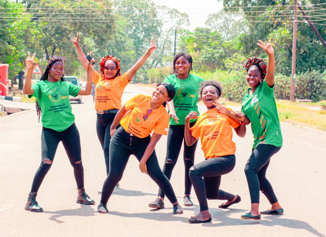 Six women wearing green and yellow t-shirts pose joyfully for a group photo outside.