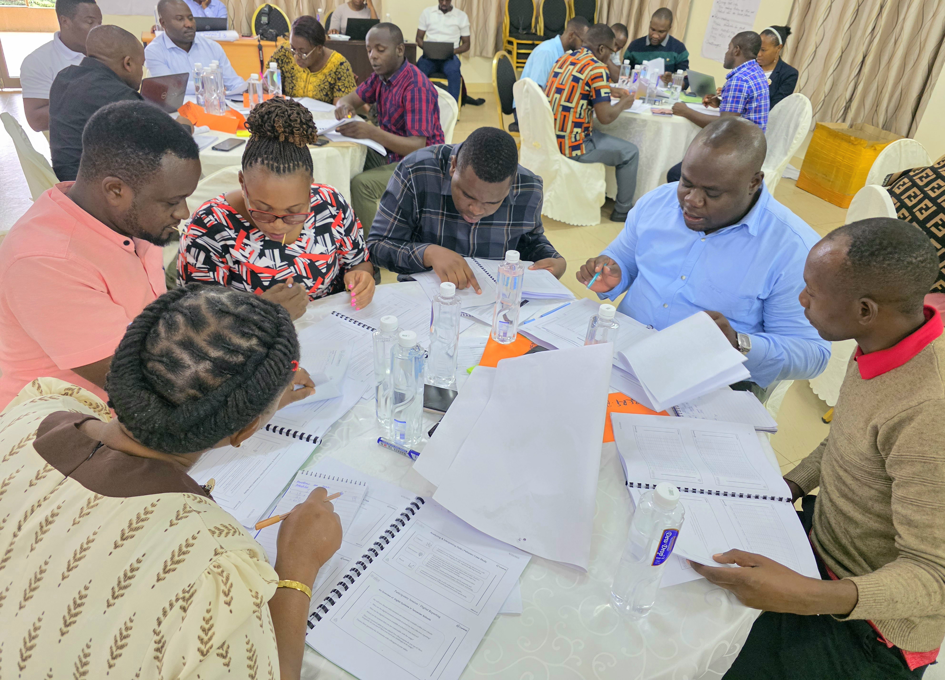 Groups of teachers gather together around round tables, looking at data sheets and research.