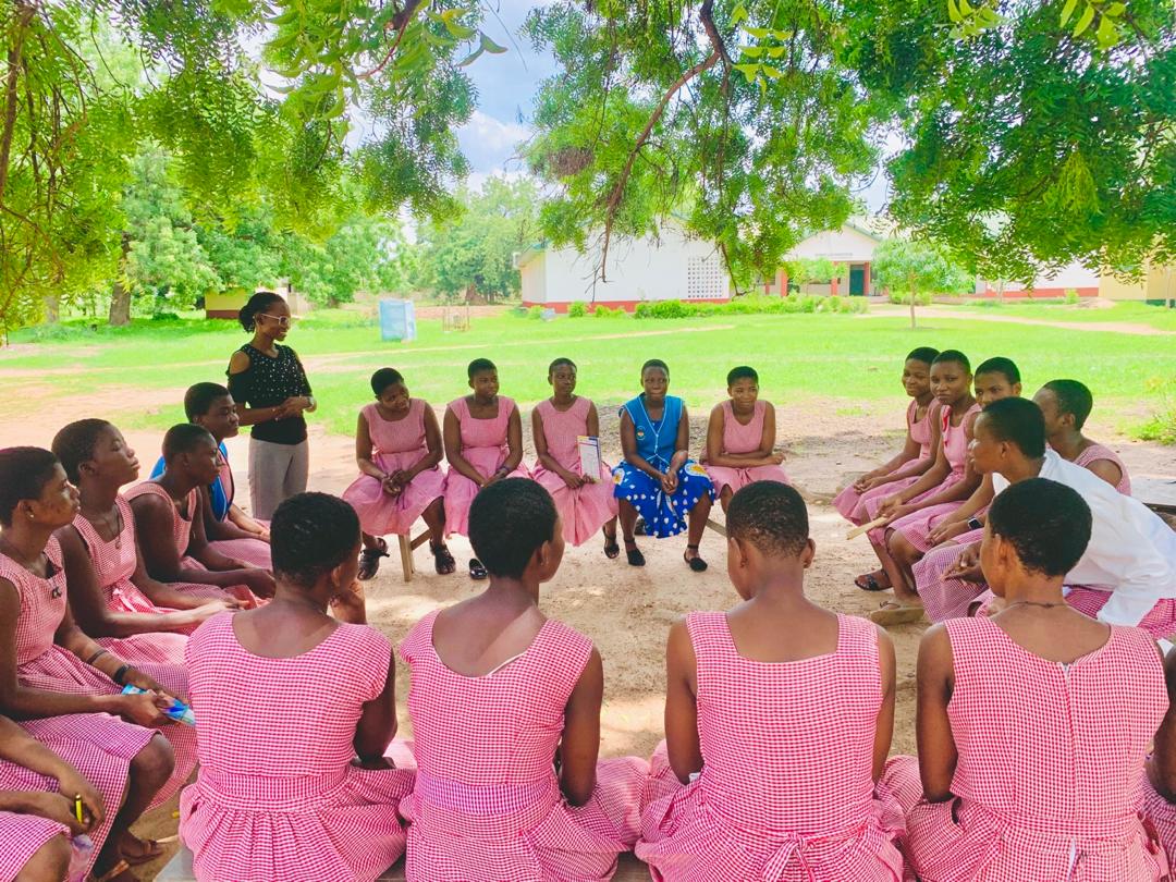 Josephine, a Ghanaian woman, leads a mentoring session for secondary students outside.