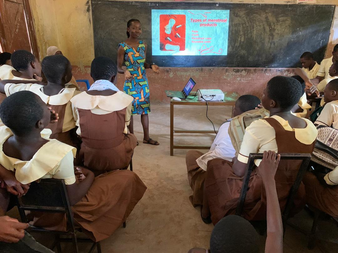 Josephine, a Ghanaian woman standing at the front of a classroom leading an SRH session for secondary students.