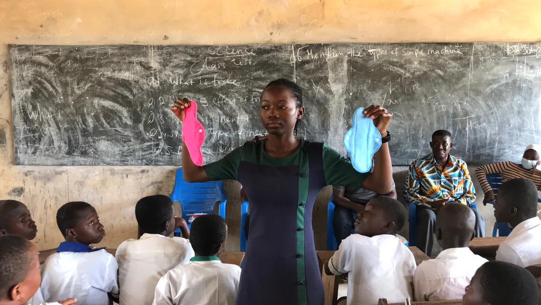 Josephine, a Ghanaian woman holding up reusable menstrual pads during a menstrual health session in a classroom with students.