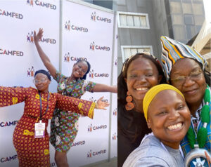 (Left photo) Blessing and Amina, two smiling Ghanaian women in patterned colorful dresses pose with their arms stretched outwards in front of a white CAMFED branded backdrop. (Right photo) Blessing and Amina smile for a selfie with Angeline Murimirwa, CAMFED CEO. 