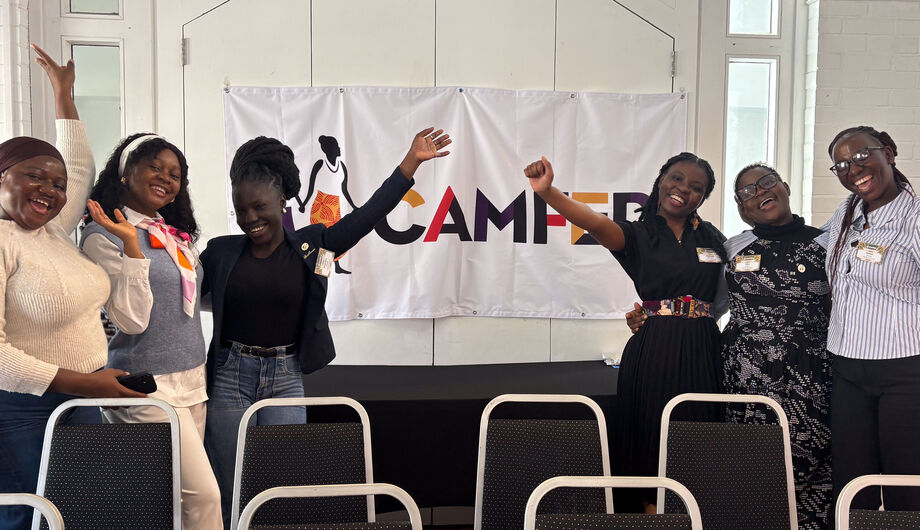 CAMFED Association members stand together smiling in front of a CAMFED banner during the Skoll World Forum, celebrating their leadership and shared commitment to education and community impact.