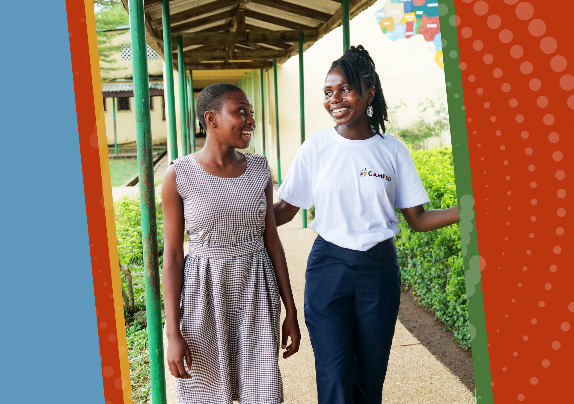 Innocent (left), a smiling Ghanaian student in school uniform, walks alongside her mentor Miss Tracy, who is wearing a white CAMFED T-shirt and dark trousers, beneath an outdoor archway on school grounds.